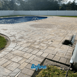 A backyard scene featuring a partially drained in-ground pool with a paved stone deck. The word "Before" is overlaid in blue text near the bottom center of the image. Surrounding the yard is a white privacy fence and some trees in the background, highlighting the need for paver restoration Nassau County services.